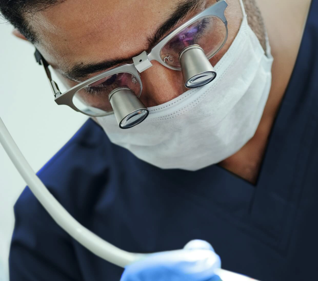 Gros plan d'un dentiste avec des loupes sur ses lunettes, penché sur la bouche d'un patient